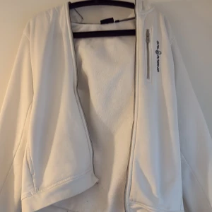 Vit fleecejacka med huva från Billabong - Säljer en vit fleecejacka från Billabong med huva och dragkedja. Jackan har en bröstficka med dragkedja och logga på framsidan. Perfekt för kyliga dagar och enkel att matcha med det mesta. Köpt för 1 år sen för 1200