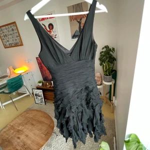 Vintage volangklänning av Shelli Segal - Supersnygg svart klänning med djup v-ringning och volangdetaljer nertill. Tillverkad i 100% silke. Klänningen har breda axelband och en figurnära passform upptill.