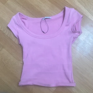 Ljusrosa croppad ribbad topp - Säljer en ljusrosa croppad topp med ribbad struktur och rundad, djup urringning. Toppen har korta ärmar och är perfekt till jeans eller kjol. Enkel och stilren design.