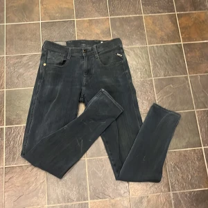 Replay Anbass svarta jeans - Säljer ett par svarta Replay Anbass jeans med klassisk femficksdesign och smal passform. Jeansen har diskreta slitningar och logotypdetalj vid fickan. Perfekta för dig som gillar stilrena och bekväma jeans.