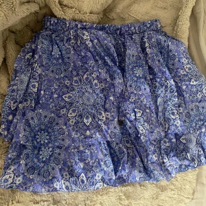 Blå mönstrad kortkjol - Supersöt blå kortkjol med vitt paisley-inspirerat mönster. Kjolen har band i midjan så man kan spänna in. Märket är off Molly så den går inte och få tag på längre☺️ storlek 1 (S) men skulle säga även M skulle passa😄 