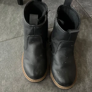 Svarta boots med dragkedja - Säljer ett par svarta boots med dragkedja på sidan och rund tå. Skorna har en ljusbrun sula som kontrast och är tillverkade i syntetmaterial. Perfekta för höst och vinter.