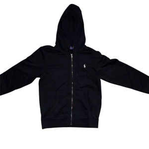 Ralph Lauren Zip Hoodie - Säljer en svart hoodie från Polo Ralph Lauren med dragkedja och huva. Tröjan har två fickor framtill och den klassiska broderade loggan i vitt på bröstet. Perfekt för en stilren och avslappnad look. 