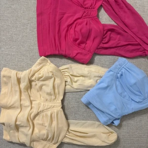 Trendig omlottopp i mesh - Säljer tre snygga omlottoppar i mesh med vadderade kupor och draperade detaljer. Finns i färgerna ceriserosa, ljusblå och ljusgul. Topparna har en axel och breda band som ger en unik look. Perfekt för att sticka ut i mängden!