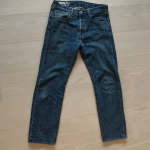 Levi's 501 blå jeansbyxor - Klassiska blå Levi's 501 jeans med raka ben och fem fickor. Byxorna har knappgylf och är tillverkade i slitstarkt denim. Perfekta för dig som gillar tidlös stil och vill ha ett par jeans som funkar till det mesta.
