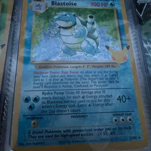 Blastoise Pokémonkort 2/102 - Säljer ett Blastoise Pokémonkort från Base Set, nummer 2/102. Kortet har blå bakgrund, holografisk yta och visar Blastoise med vattenkanoner på ryggen. Text och HP i rött och svart, samt Pokémon-logga i hörnet. 1995