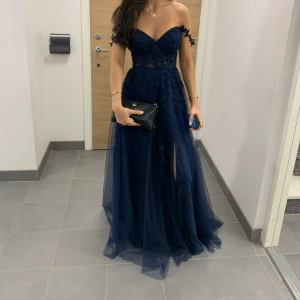 Balklänning - Marinblå långklänning med spetsdetaljer - BALKLÄNNING Elegant marinblå långklänning med spetsdetaljer och en slits framtill. Klänningen har en offshoulder-design med dekorativa axelband och en v-ringad urringning. Jag är 165 på bilden + klackskor ca 6 cm🤩