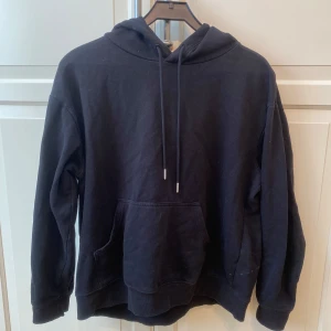 Svart hoodie från H&M - En klassisk svart hoodie från H&M med huva och dragsko. Tröjan har en stor magficka framtill och ribbade muddar vid ärmslut och nederkant, tröjan är i strl M