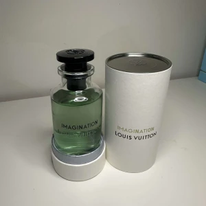 Imagination parfym från Louis Vuitton - Lyxig parfymflaska från Louis Vuitton, modell Imagination. Flaskan är genomskinlig med ljusgrön vätska och svart rund kork. Kommer i elegant vit cylinderförpackning med silverdetaljer och tryckt logga.