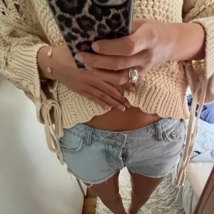 Ljusblå jeansshorts med fransar - Säljer ett par ljusblå jeansshorts med råa franskantade benslut och klassisk femficksdesign. Shortsen har låg midja och en avslappnad passform, perfekta för varma dagar.