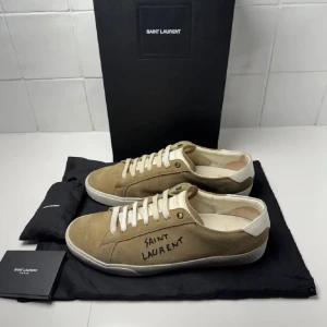 Saint Laurent skor - Snygga beige sneakers från Saint Laurent med vit sula och snörning. Skorna har en stilren design med Saint Laurent-logga på sidan. Perfekta för en avslappnad och trendig look. Inget og vid köp. Bara att höra av sig till oss vid minsta fundering😁 OBS Låda och dustbag kommer inte vid köp. Sulan är omfärgad till vit den är beige orginellt men om de tappar färg e de bara att färga de igen med solecolor eller rocka den  Orginal färgen på sulan