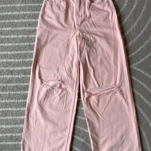 Ljusrosa jeans med slitningar - Säljer ett par ljusrosa jeans från STAY med raka ben baggy ben och slitna detaljer vid knäna. Klassisk femficksmodell med knapp och dragkedja i midjan. Perfekta för dig som vill ha en trendig och avslappnad look.