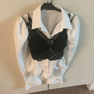 Svart spetsig croppad linnetopp - Säljer en svart croppad linnetopp i spets med tunna axelband och snyggt mönster. Perfekt att styla över en skjorta eller bära som den är. Toppen har ett feminint och trendigt utseende med fina detaljer.