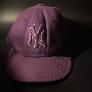 Lila New York Yankees keps - Säljer en lila keps från New Era med New York Yankees-logga broderad framtill. Klassisk böjd skärm och justerbar passform. Perfekt accessoar för att lyfta din stil.