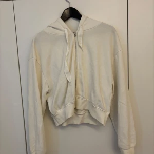Vit hoodie med dragkedja från Bik Bok - Säljer en vit hoodie från Bik Bok i storlek M. Tröjan har dragkedja framtill, huva med snören och är croppad i modellen.
