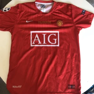 Manchester United Ronaldo 7 Finaltröja - Klassisk röd Manchester United fotbollströja, Nike med AIG som sponsor, Champions League-finalen i Moskva 2008 tryckt på bröstet och Ronaldo 7 på ryggen. Kortärmad modell i lätt och ventilerande material, perfekt för fotbollsälskare och samlare.