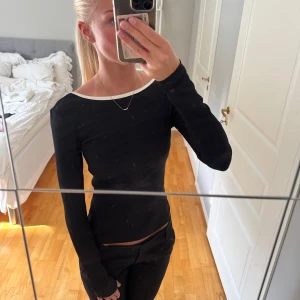 Svart ribbad långärmad topp med vit kant - Svart långärmad topp med vit kant runt halsringningen och ryggen. Toppen är ribbad och har en snygg öppen rygg. Figurnära passform som sitter tajt och snyggt. Aldrig använd💕