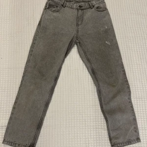 Gråa grunt raka jeans i vintage-stil - Snygga grå jeans med rak passform och klassisk femficksdesign. Jeansen har en enkel look utan synliga loggor och är perfekta för dig som gillar en clean och avslappnad stil. Materialet är robust denim och färgen är en tvättad grå nyans.