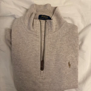 Beige half zip tröja från Polo Ralph Lauren - Snygg beige tröja från Polo Ralph Lauren med half zip och klassisk ståkrage. Tröjan har det ikoniska broderade logot på bröstet och är tillverkad i mjuk bomull. Perfekt för lager-på-lager och chill stil.
