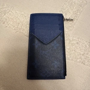 Blå Louis Vuitton plånbok i skinn - Säljer en blå plånbok från Louis Vuitton i skinn med klassiskt monogrammönster. Plånboken har flera kortfack, dragkedja i silver och en stilren, avlång form. Perfekt för dig som vill ha något lyxigt och snyggt i väskan.