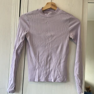 Ljuslila ribbad långärmad tröja Monki - Supersnygg ljuslila långärmad tröja från Monki i ribbad bomull. Tröjan har en enkel, tight passform och rund halsringning. Perfekt att styla med jeans eller kjol för en chill look. Storlek XS.