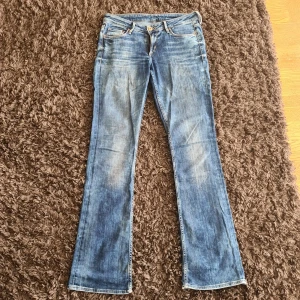 Bootcut jeans från H&M, ljusblå - Bootcut jeans från H&M i en snygg ljusblå tvätt med slitningar och klassiska fem fickor. Låg midja och långa ben med utställd passform nertill. Tillverkade i bomull med dragkedja och knapp framtill. Perfekta för en avslappnad och trendig look.