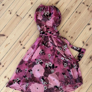 Blommig rosa silkesklänning Twist & Tango - Supersöt kort klänning från Twist & Tango i 100% silke. Klänningen är rosa med stora blommiga mönster i svart och vitt, har knyt i midjan och axelbandslös design. Perfekt för dig som vill sticka ut med färg och mönster. Sval och lyxig känsla!