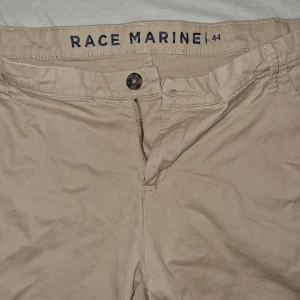 Beige shorts från Race Marine - Snygga beige shorts från Race Marine med klassisk passform. De har fickor fram och bak, bälteshällor och stängs med knapp och dragkedja. Perfekta för varma dagar och enkla att matcha med det mesta. Materialet känns mjukt och skönt mot huden.