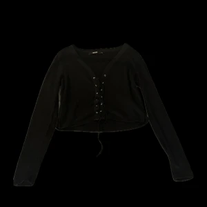 Svart tröja  - En fin tröja med snören där fram som man kan knyta till en rosett eller vad som. Aldrig använt. Axelbredd-40cm. Längd-41cm.