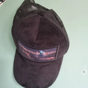 Svart keps med New York-tryck - Snygg svart keps med mesh på sidorna och justerbar snapback. Framtill finns ett coolt tryck med Frihetsgudinnan och New Yorks skyline. Framsidan är i mjukt material som känns lyxigt. Perfekt för dig som gillar streetstyle och vill sticka ut.