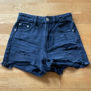Svarta jeansshorts Stradivarius - Snygga svarta jeansshorts från Stradivarius med hög midja och råa, slitna detaljer. Klassisk femficksmodell med fransig kant och coola slitningar både fram och bak. Perfekta för en chill och trendig look i sommar.
