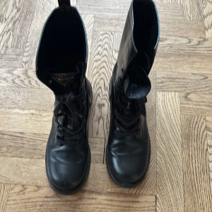 Svarta boots från Louis Vuitton - Snygga svarta boots från Louis Vuitton i skinn med klassiska monogramdetaljer i brunt på plösen och baktill. Skorna har snörning framtill och en robust platt sula. Perfekta för dig som vill ha en lyxig och edgy look.
