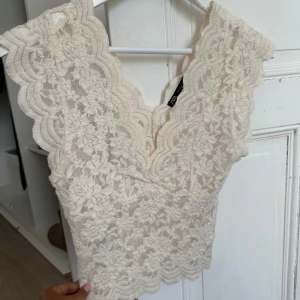 Vit spetsblus från Zara - Slutsåld Superfin vit blus från Zara i spets med v-ringning och ärmlös design. Blusen har vackra blommiga spetsdetaljer och vågig kant nertill och vid axlarna. Perfekt för dig som gillar romantisk och feminin stil.