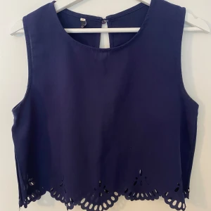 Mörkblå topp med broderad kant - Snygg mörkblå ärmlös topp med rund halsringning och dekorativt broderad och utskuren kant nertill. Tunt material och lätt kroppad. M men sitter mer som en S.