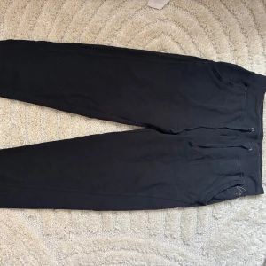 Svarta mjukisbyxor från Clique M - Svarta mjukisbyxor från Clique med ribbade muddar i midja och benslut. Byxorna har snörning i midjan och broderad logga på ena benet. Perfekta för chill eller träning, riktigt sköna och stilrena.