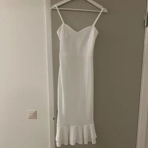 Vit klänning - Snygg vit midiklänning med smala axelband och volangdetalj längst ner. Enkel och stilren look som känns både fräsch och trendig. Har bara använts och tvättats en gång. Klänningen är även stretchig. Passar för strl. S o M 