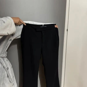 Svarta lågmidjade kostymbyxor från Zara - Stilrena svarta lågmidjade kostymbyxor från Zara Woman med klassisk rak passform och diskreta fickor bak. Byxorna har en låg midja och är perfekta för en clean och snygg look. Materialet är mjukt och följsamt, vilket gör dem riktigt bekväma.