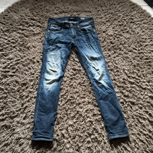 Blå slim jeans från Replay - Säljer ett par blå slim fit jeans från Replay med klassisk femficksdesign och snygga tvätt på framsidan. Jeansen har normal midja och är tillverkade i mjukt denimtyg med tydliga kontrastsömmar och läderpatch bak i midjan.