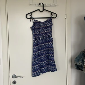 Blå mönstrad sommarklänning med smala axelband - Säljer en kort blå klänning med smala axelband. Det är lite kort så man tänker på det+ axelband kan justeras om man tar ut knutarna 
