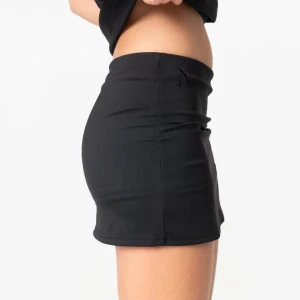 Svart sportig minikjol från Nitted - Svart tight minikjol från Nitted med inbyggda shorts under. Kjolen är stretchig och gjord i mjukt material med 75% polyester och 25% spandex. Perfekt för dig som vill ha en sportig och bekväm look. Enkel design utan mönster eller detaljer.
