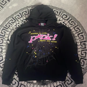 SPCS hoodie - Cool svart hoodie från SPCS Design med färgglatt tryck framtill, spindelnätsmotiv och texten 'prank!'. Hoodien har huva och långa ärmar, perfekt för dig som gillar unika och lekfulla plagg.