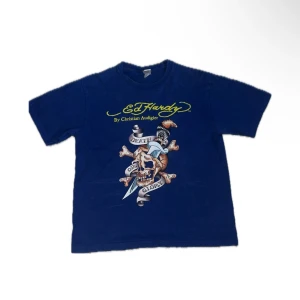 Blå Ed Hardy t-shirt med tryck - Snygg blå t-shirt från Ed Hardy med stort dödskalle- och örntryck på framsidan och coolt logotryck på ryggen. Modellen är klassisk med rund hals och korta ärmar. Materialet är mjuk bomull, perfekt för dig som gillar statement-plagg.