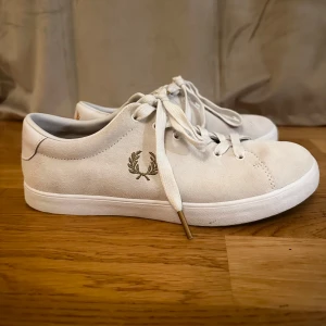 Sneakers från Fred Perry mocka - Vita sneakers från Fred Perry i mocka med klassisk Fred Perry-logga broderad i guld på sidan och hälen. Skorna har vita snören med gulddetaljer. Endast använd två gånger men var för stora i storleken för mig😅Väldigt rena!🥰