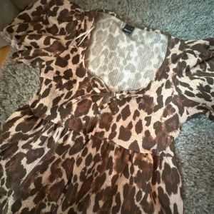 Leopardmönstrad topp med puffärm - Snygg topp från Gina med leopardmönster i brunt och beige. Toppen har puffiga korta ärmar med knyt fram och lätt rynkad midja för en avslappnad men trendig look. 