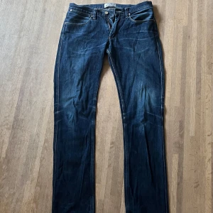 Mörkblå jeans från Acne Studios - Snygga mörkblå jeans från Acne Studios med klassisk femficksdesign och raka ben. Jeansen har orangea kontrastsömmar, bälteshällor och dragkedja framtill. Perfekta för dig som gillar stilrena och tidlösa jeans i denim.