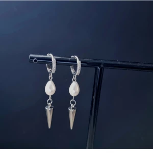 Silvriga örhängen med pärlor och spikes - Snygga örhängen i silverfärg med droppformade vita pärlor och coola spetsiga spikes som hänger ned. Perfekt för dig som gillar att sticka ut med din stil och vill ha något unikt till öronen.