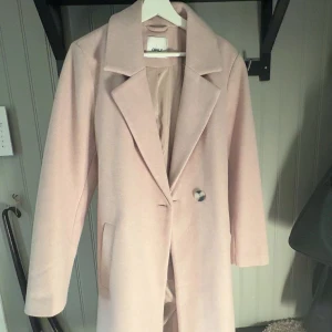 Beige kappa från ONLY med bälte - Säljer en stilren beige kappa från ONLY med klassisk krage, knäppning framtill och bälte i midjan. Jackan har långa ärmar och två fickor framtill. Perfekt för dig som vill ha en clean och trendig look under höst och vinter i storlek XL men är liten i storleken! Passar mig som har storlek s-m osv💕