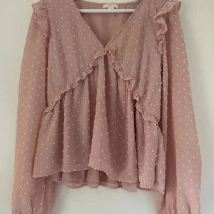 Rosa volangblus  - Supersöt rosa blus med volangdetaljer och små prickar i tyget. Blusen har v-ringning, lång ärm och ett luftigt, flowy fall. tröjan är i 170 alltså ungefär xs/s