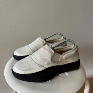 Y-3 slip-on sneakers med platåsula - Unika slip-on sneakers från Y-3 i beige canvas med svart platåsula. Snygg minimalistisk design med Y-3 logga framtill och svart detalj baktill. Skorna har rund tå och platt, hög sula som ger extra edge till din stil.