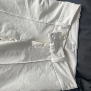 Vita kostymbyxor från Gina Tricot - Snygga vita kostymbyxor från Gina Tricot i storlek 158. Byxorna har raka ben, bälteshällor och stängs med knapp och dragkedja. Perfekta för en clean och stilren look. Tillverkade i mjukt bomullsmaterial.